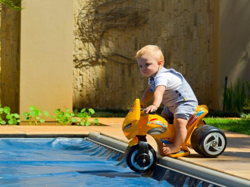 A child on a toy bike beside a pool with the cover closed
