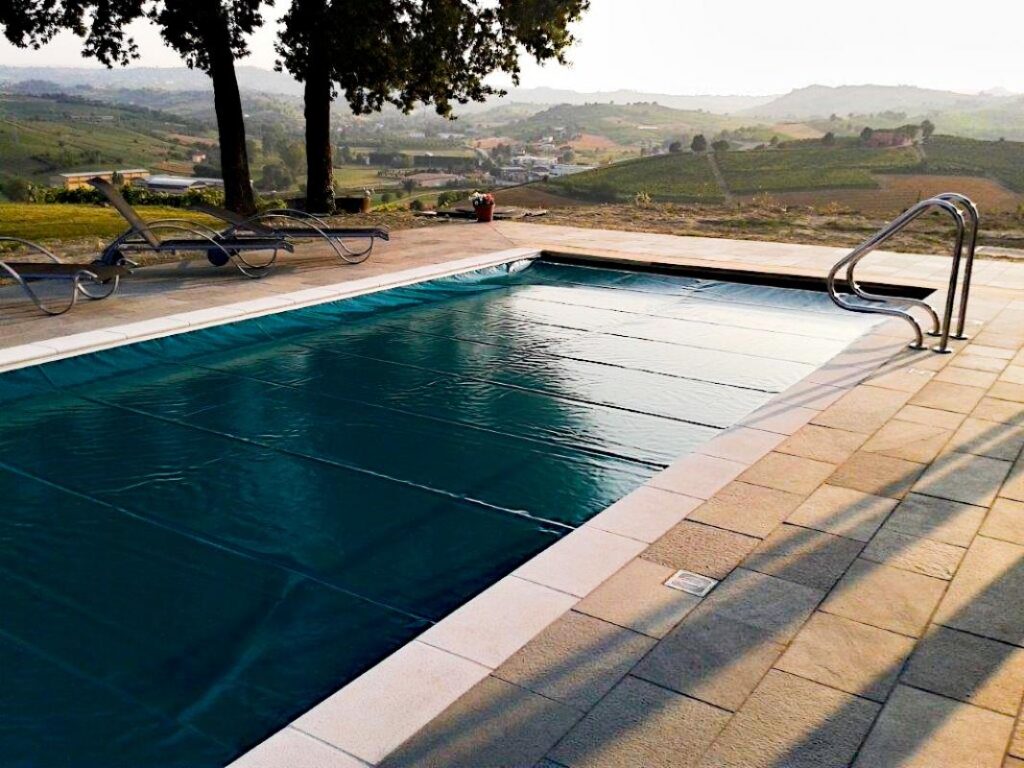 A safety cover closed over a hillside pool at dusk, a stainless ladder at the near corner