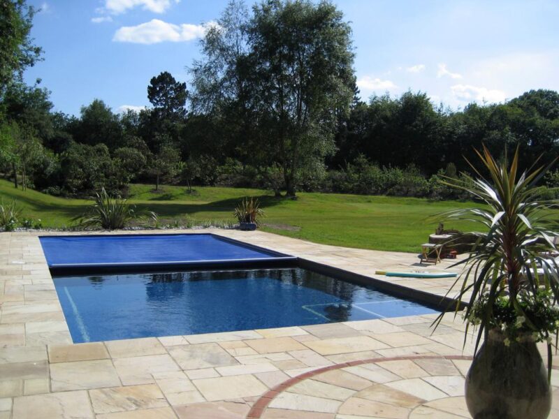 A dark blue safety cover closed across an outdoor pool in an English garden, the water still visible at the near end