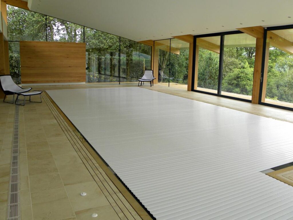 A white slatted cover closed across an indoor pool, in a timber and glass pool house