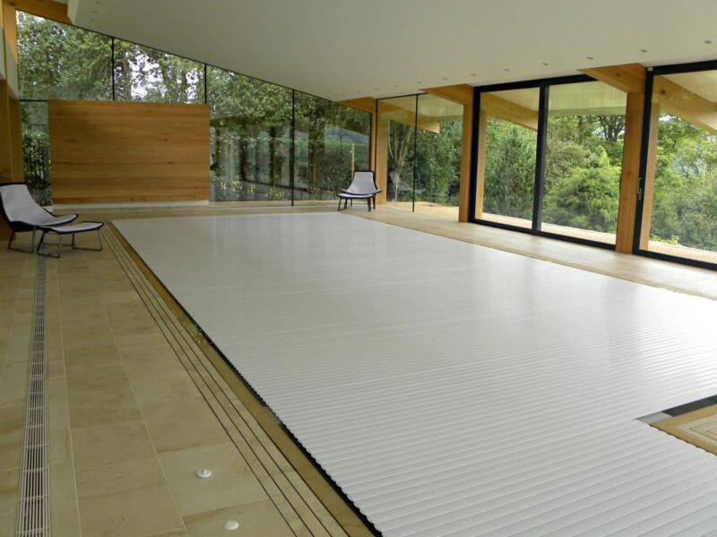 A white slatted cover closed across an indoor pool, in a timber and glass pool house