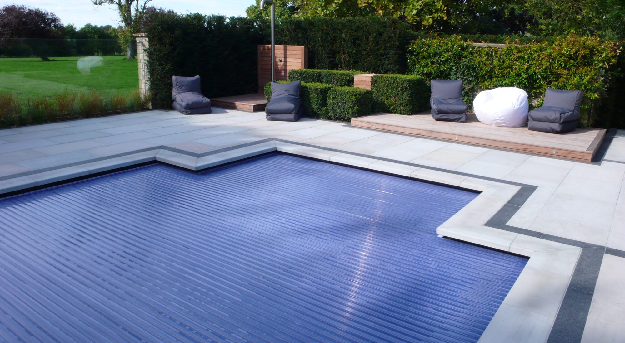 A slatted cover closed across a pool in an English garden, the slats running the length of the water