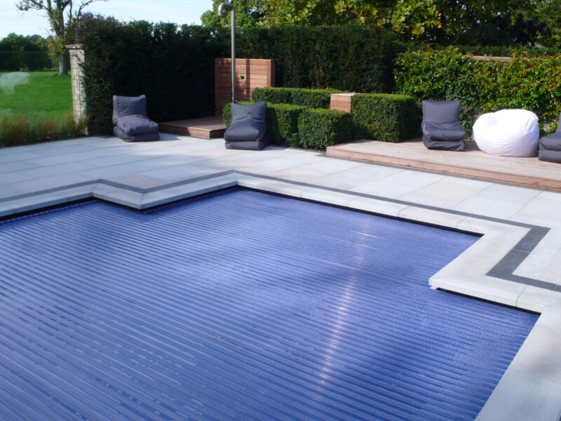 A slatted cover closed across a pool in an English garden, the slats running the length of the water