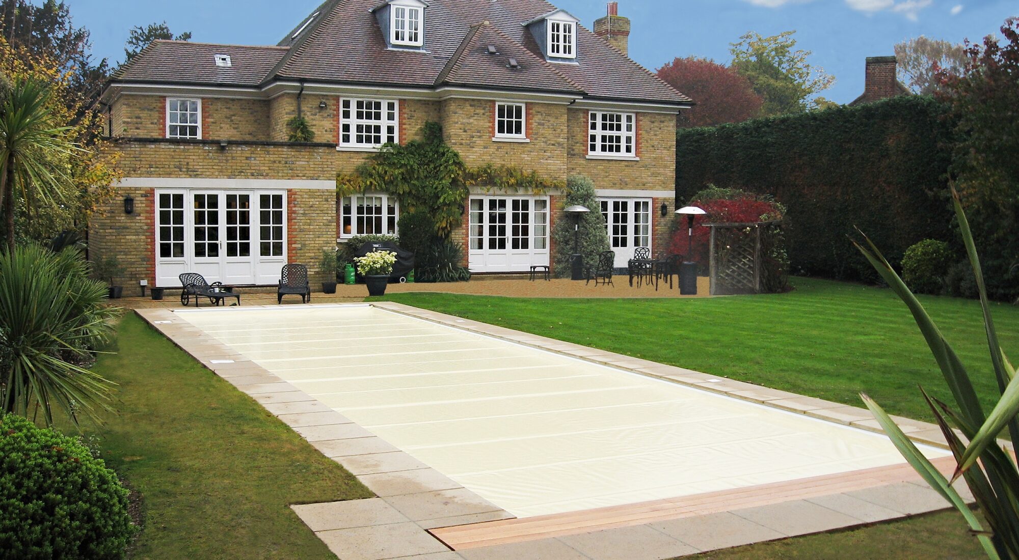 A PoolLock safety cover closed over a domestic pool in an English garden in autumn.